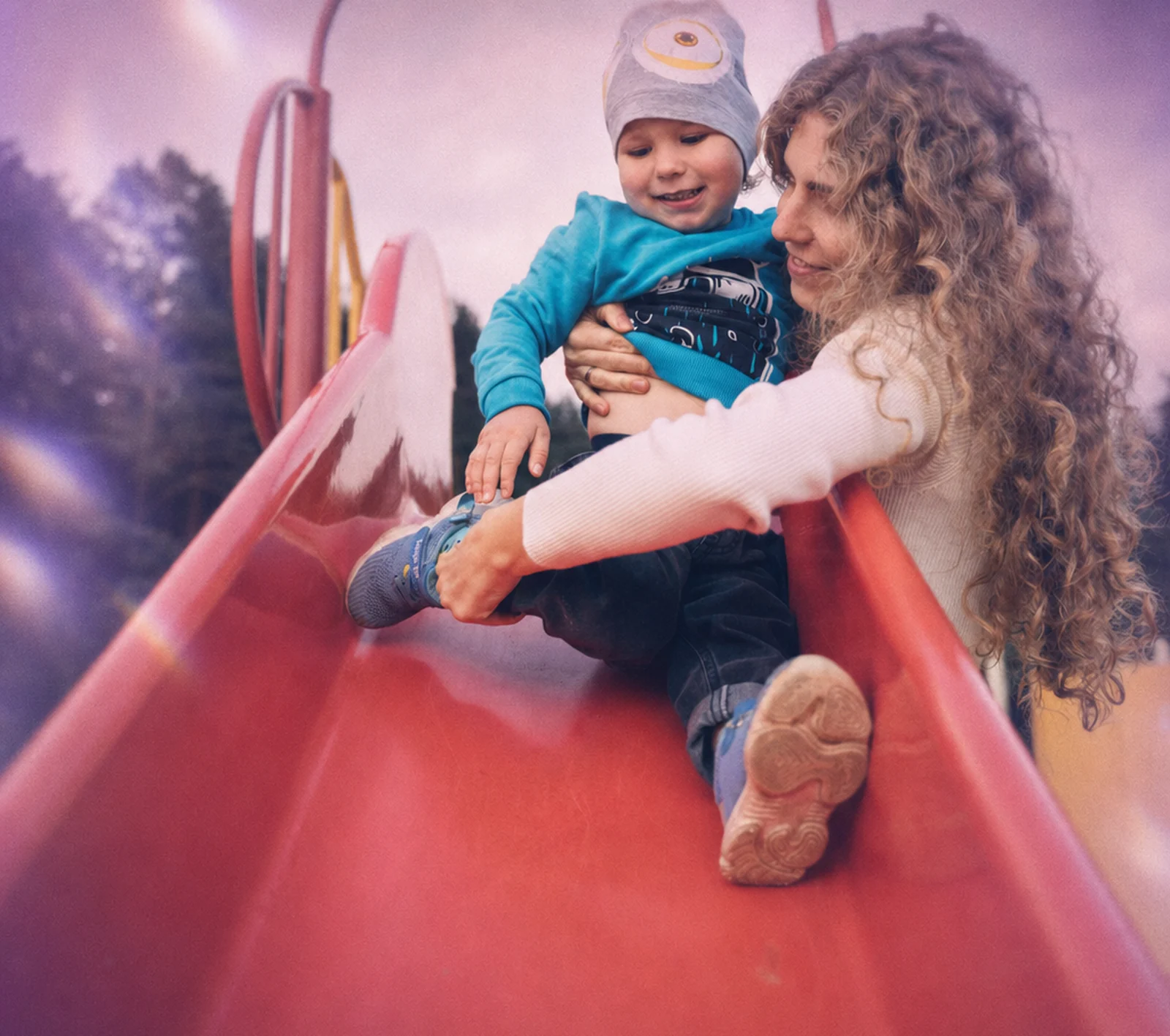 A parent waving during a virtual ABA session while her toddler plays beside her