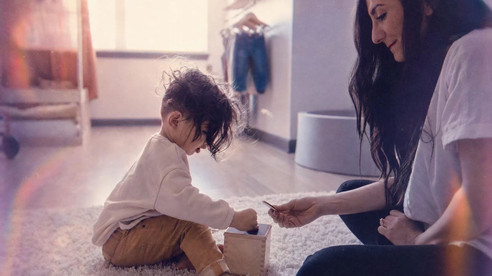 A parent and toddler play with a shape-sorting box on a living room rug