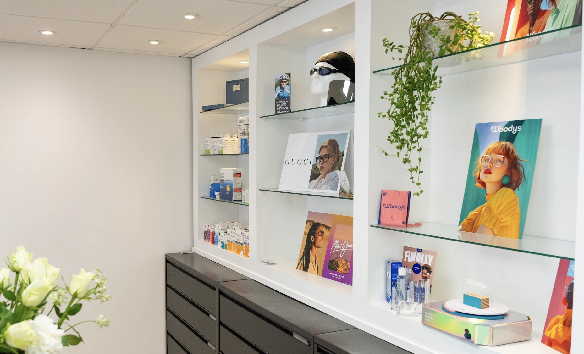 Modern optician practice interior featuring eyewear displays, designer frame collections, eye care products, and bright contemporary shelving