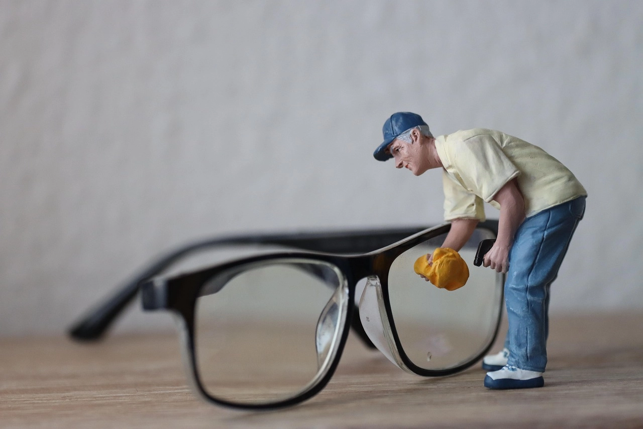 Miniature worker cleaning the lens of a pair of eyeglasses, symbolising eyewear maintenance, lens care, and clear vision