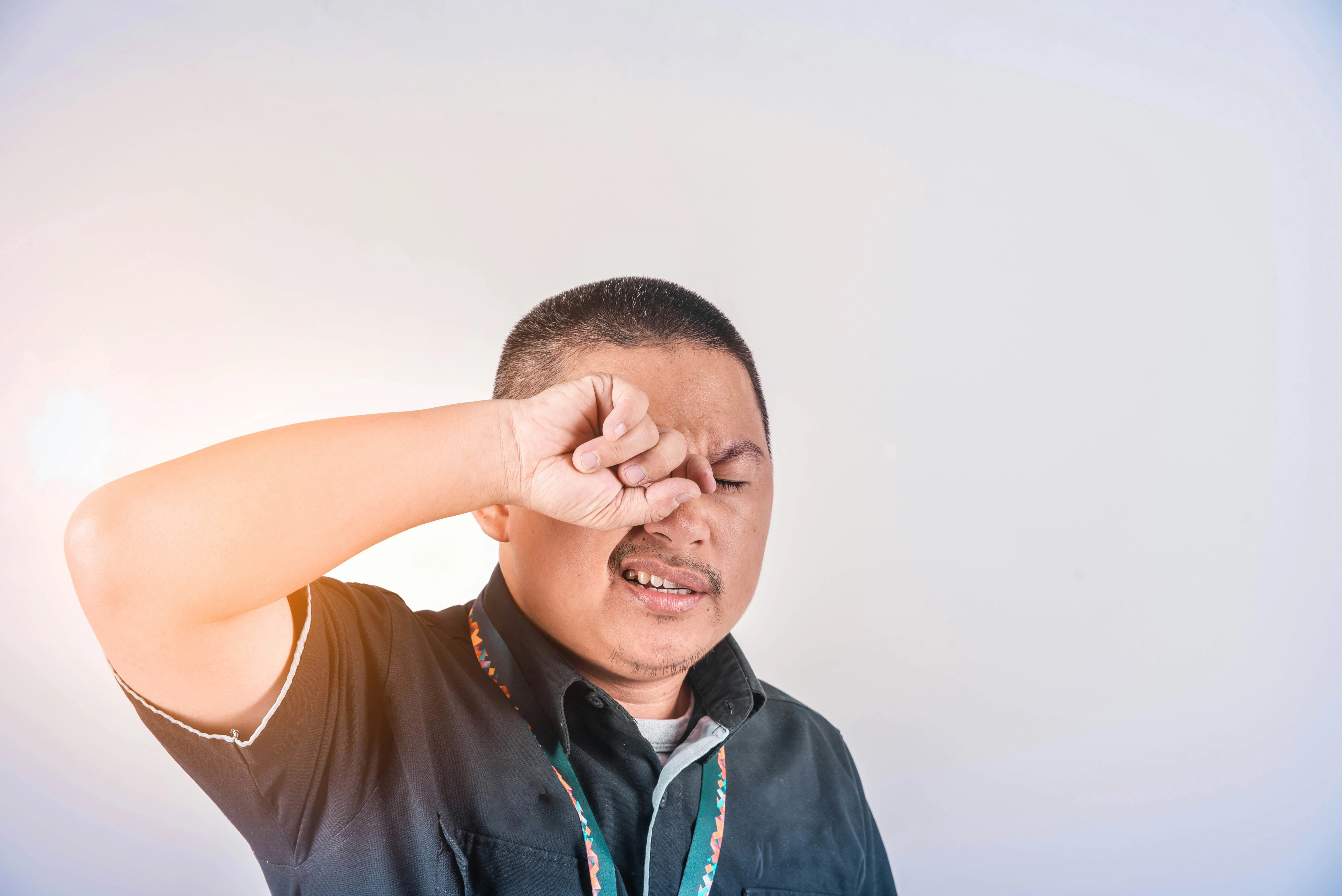 Man rubbing his eye with his forearm, showing signs of eye irritation, discomfort, or fatigue against a plain background