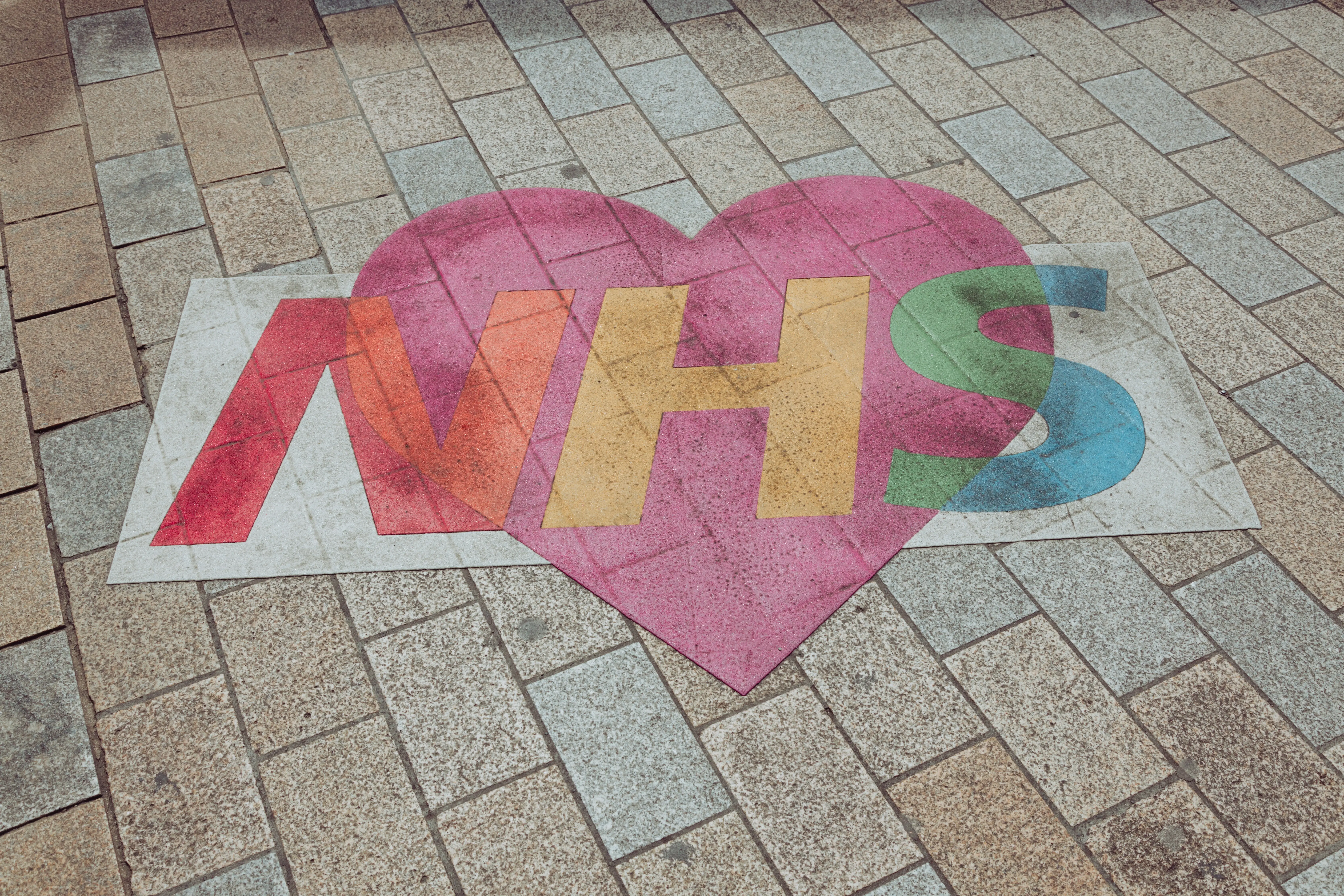 Colourful NHS heart logo displayed on a paved walkway, highlighting support for the National Health Service and community healthcare