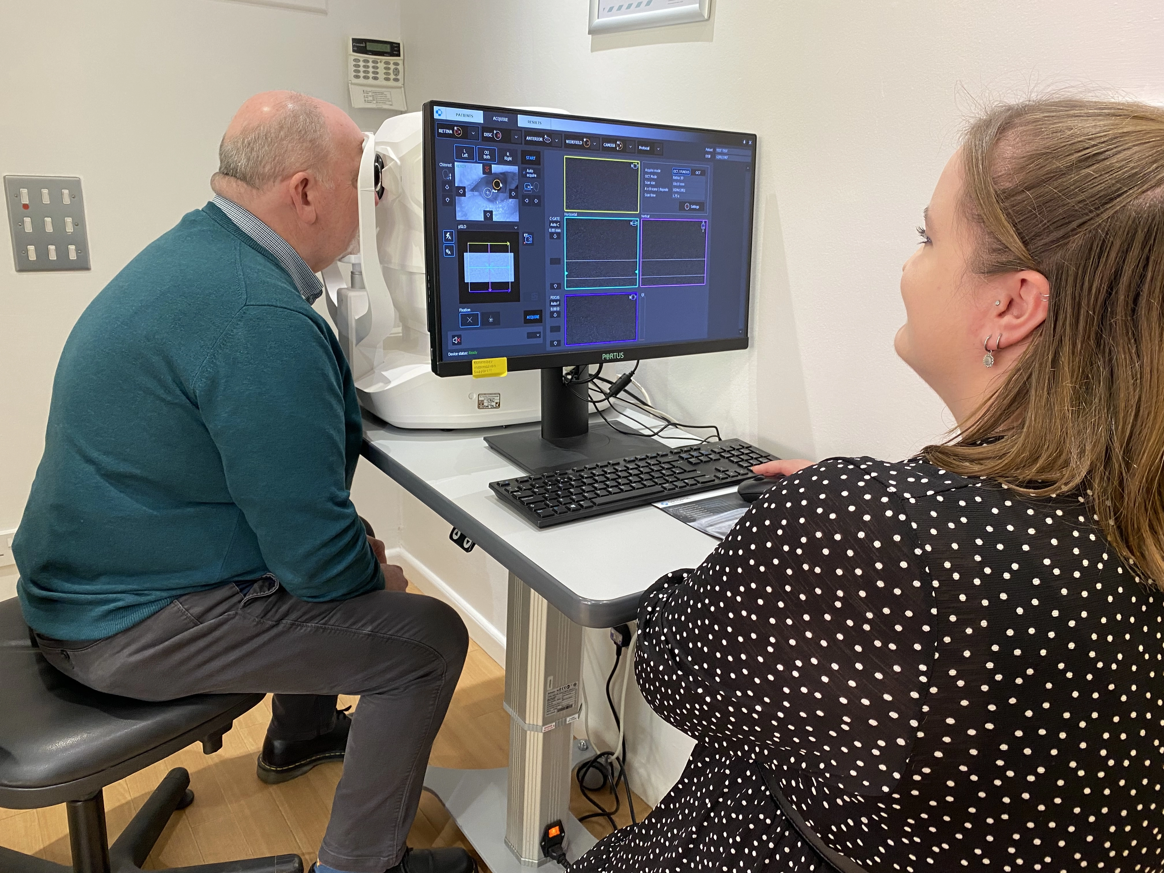 Patient undergoing an advanced eye scan while an optician reviews retinal imaging results on a computer screen during an eye examination