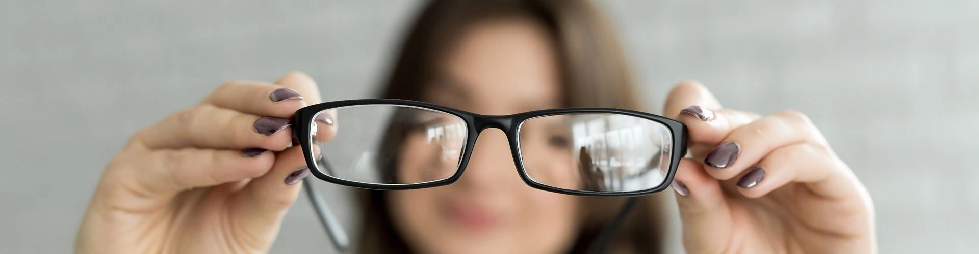 Person holding a pair of eyeglasses in front of their face, demonstrating blurred vision and the importance of corrective lenses