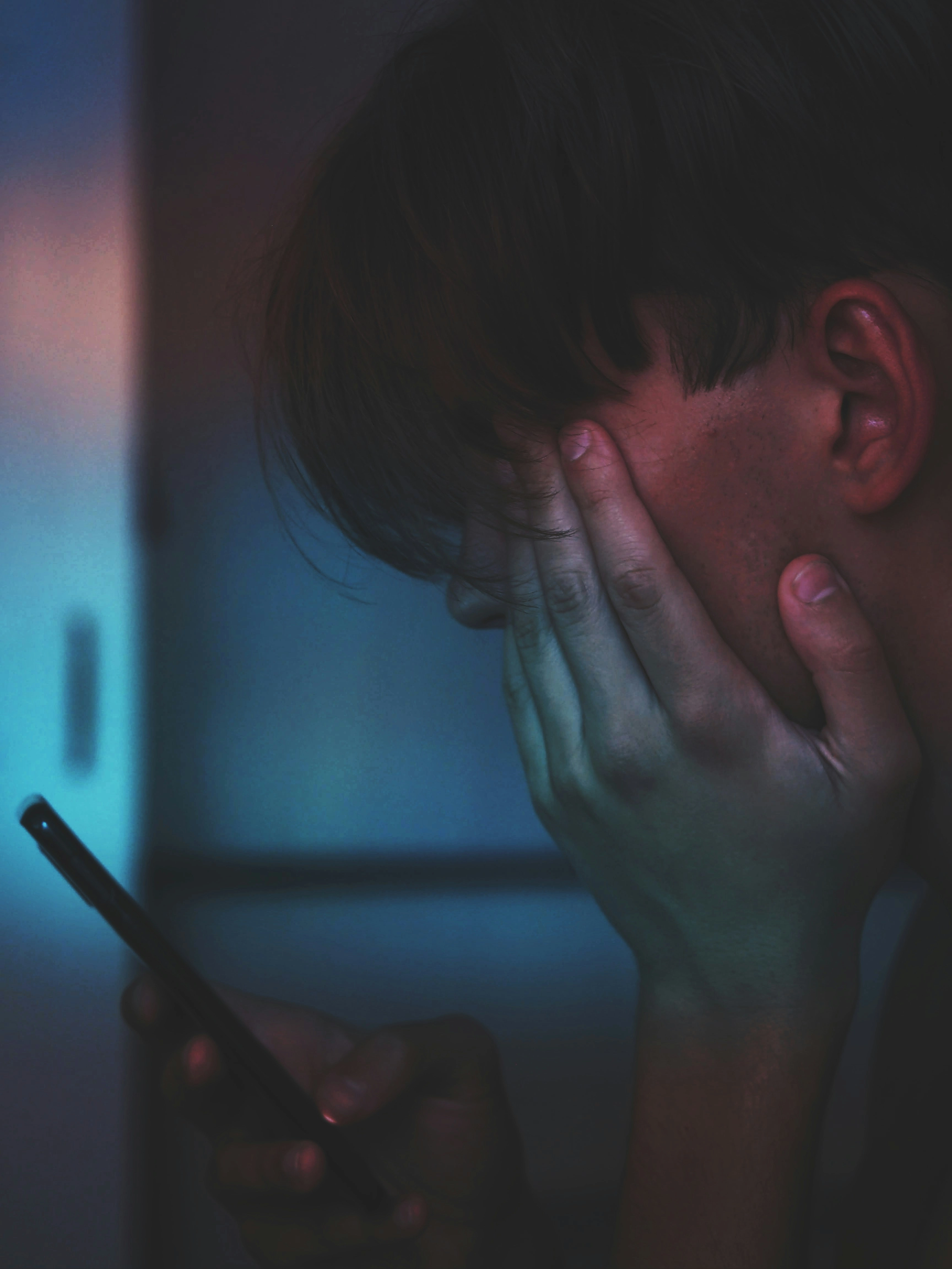 Person looking at a smartphone in a dimly lit room while rubbing their eye, illustrating digital eye strain and screen fatigue