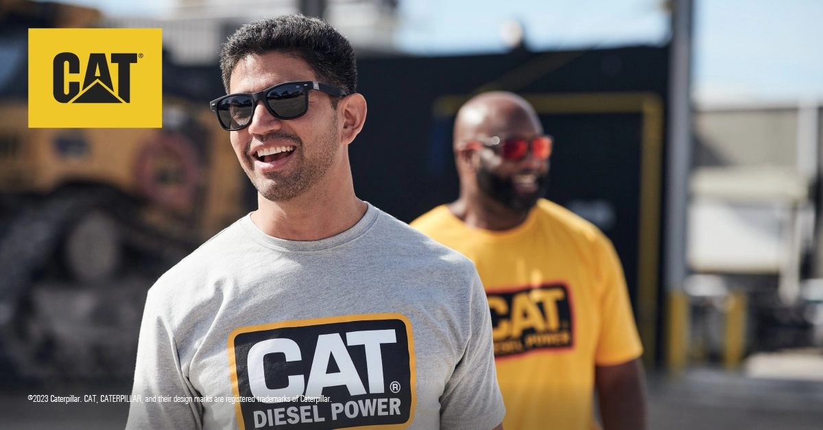 Two people wearing CAT-branded sunglasses and apparel outdoors at an industrial worksite on a sunny day