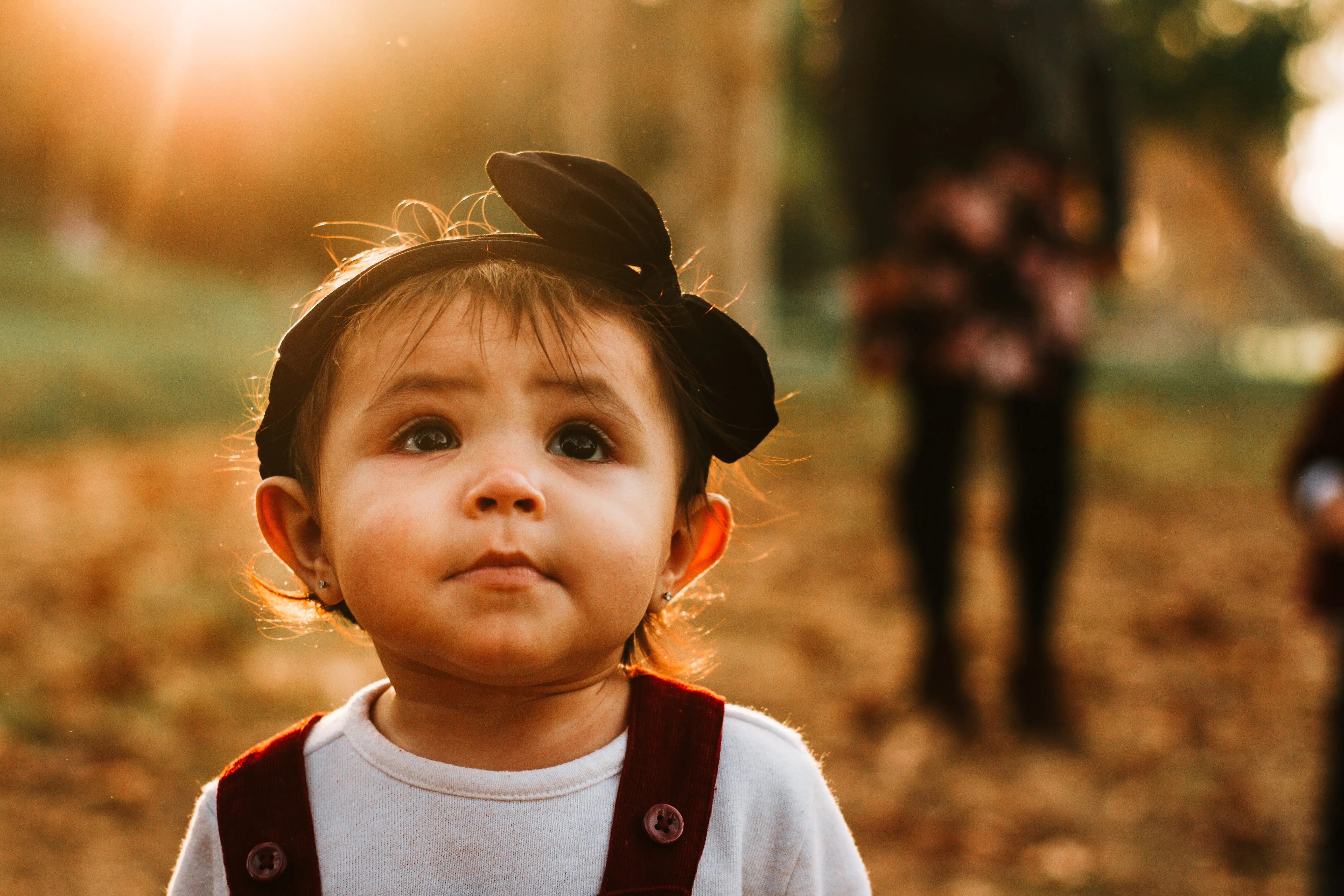 Young child outdoors during golden hour, looking up with bright eyes and a curious expression in a warm autumn setting