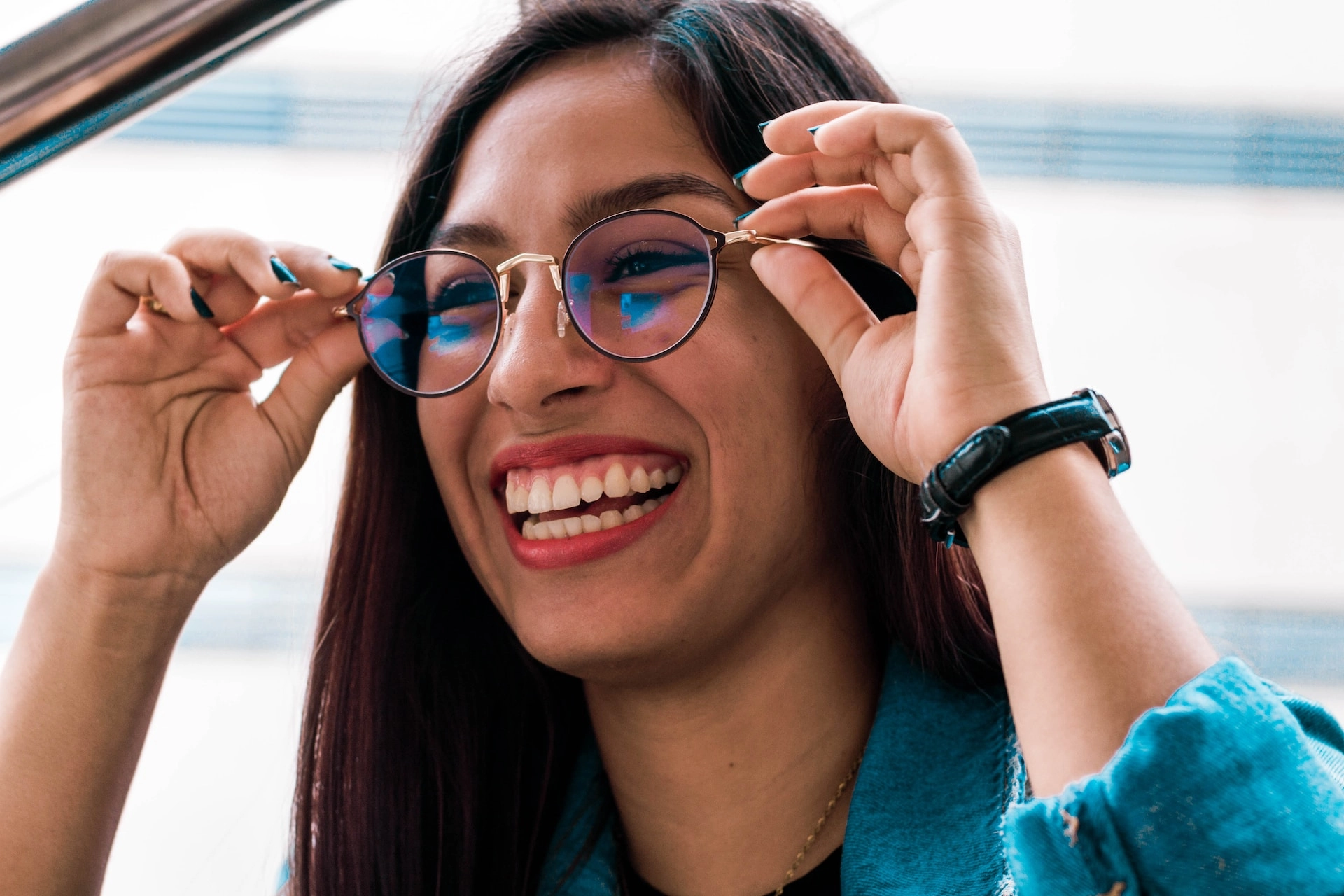 Smiling woman adjusting a pair of stylish round eyeglasses while enjoying clear vision and comfortable eyewear