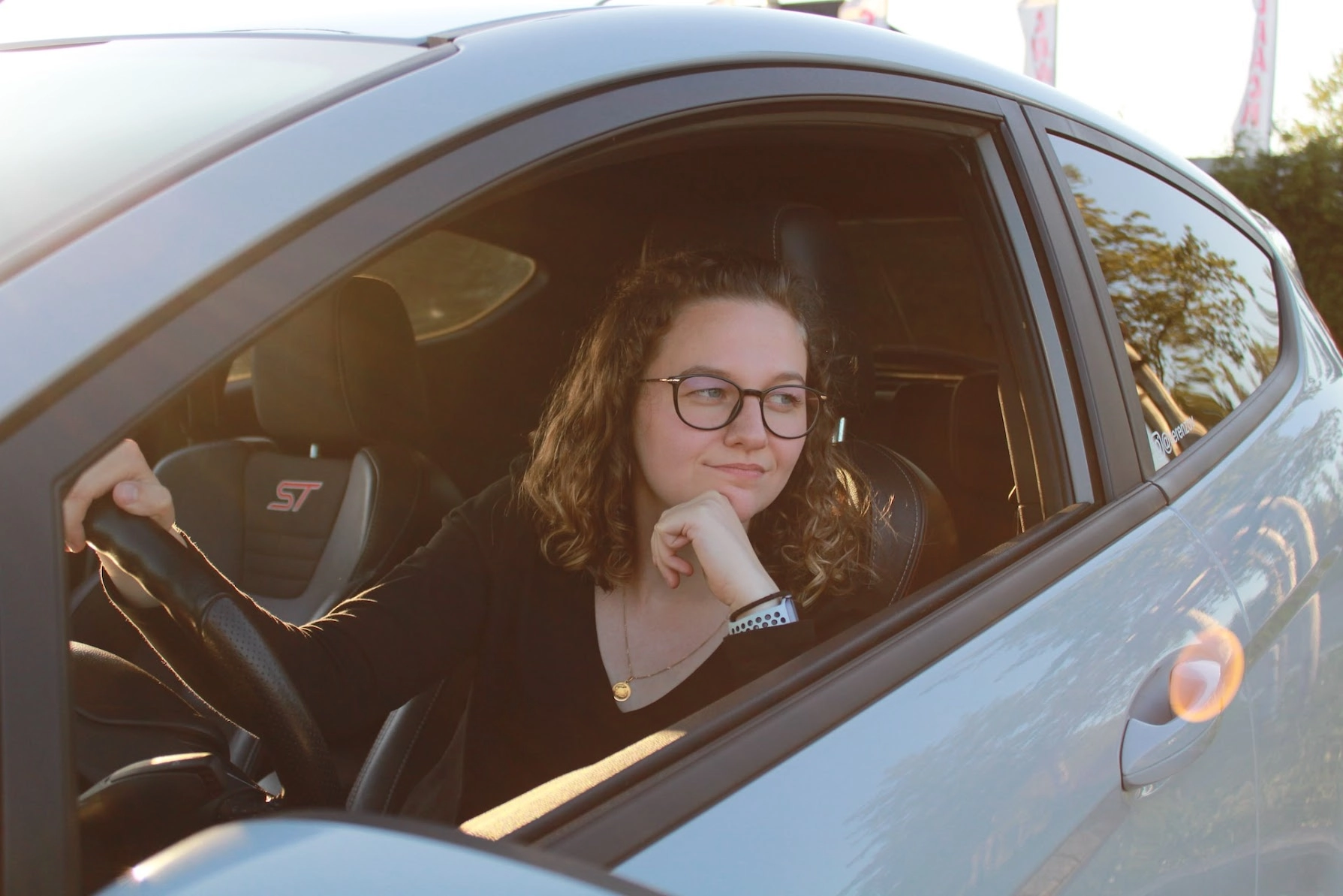 Person wearing prescription glasses sitting in the driver's seat of a car and looking out of the open window