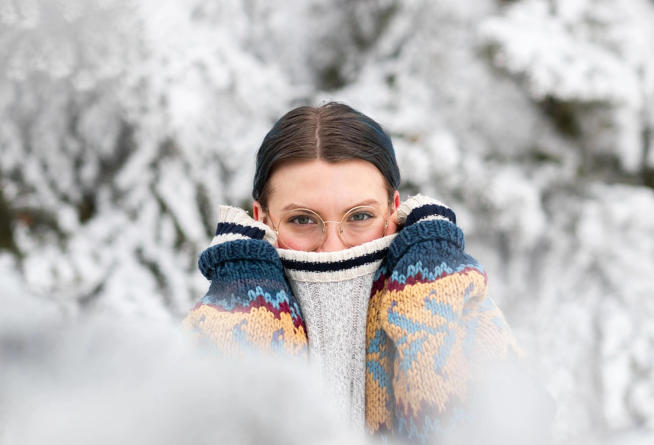 Person wearing round eyeglasses and a colourful winter sweater outdoors in a snowy landscape