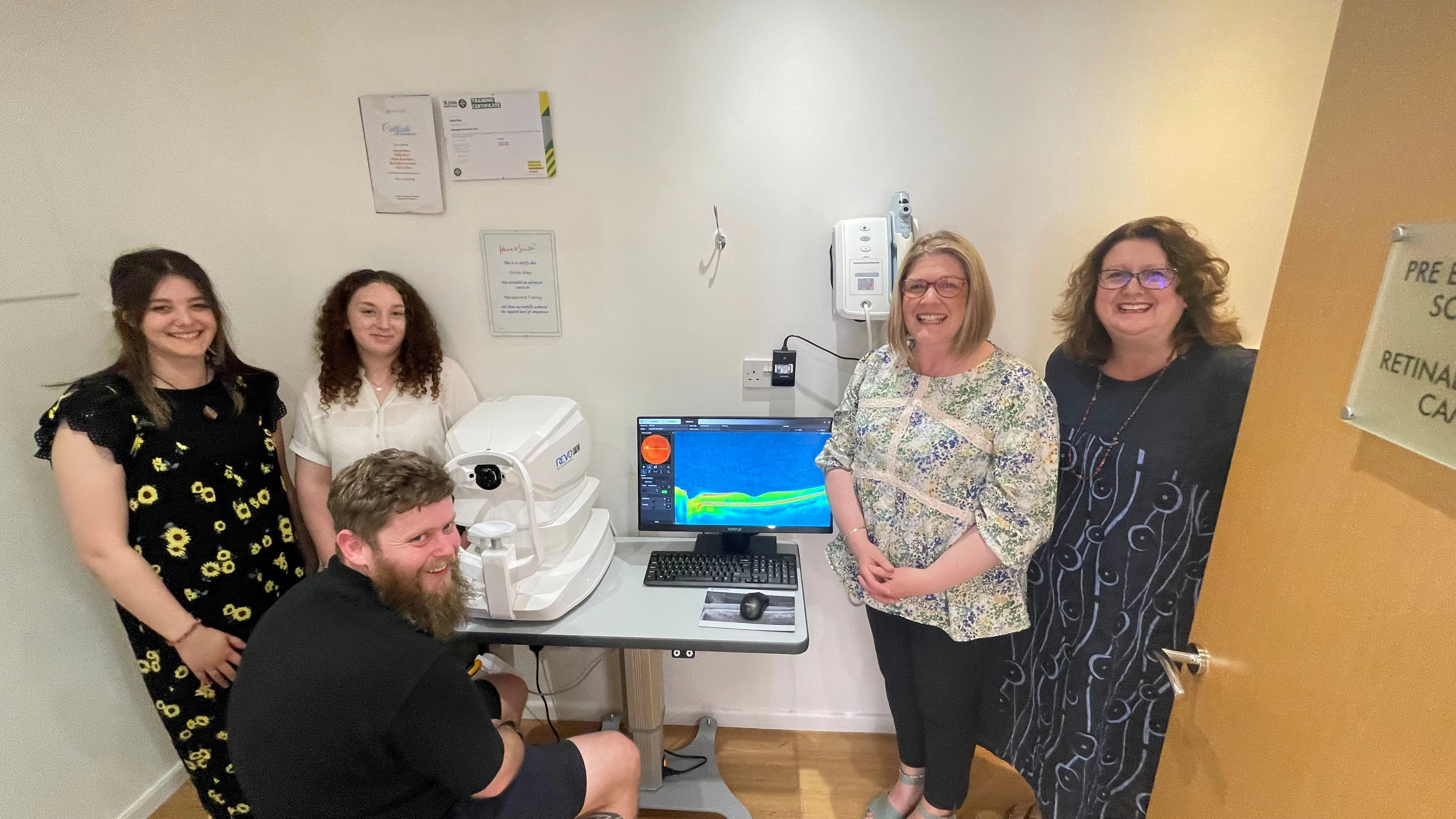 Optical practice team gathered around advanced retinal imaging equipment in a clinical examination room