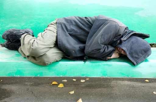 Person experiencing homelessness sleeping on a green public bench