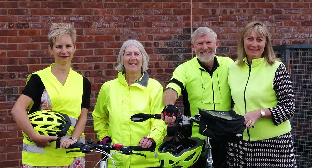 Four cyclists in high-visibility jackets posing with bicycles and safety helmets