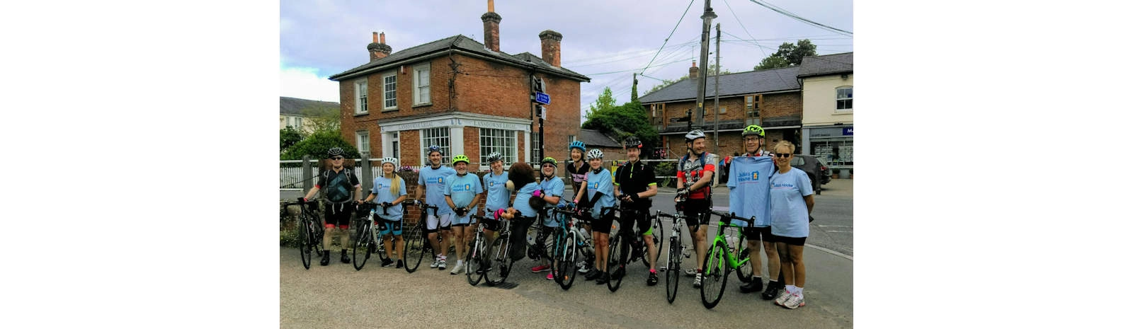 Group of cyclists posing with their bicycles in a village square during a community fundraising ride