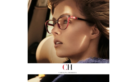 Close-up of a woman wearing stylish red Carolina Herrera eyeglass frames, photographed in warm natural light