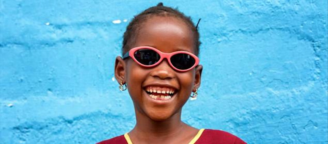 Smiling child wearing pink sunglasses against a bright blue wall