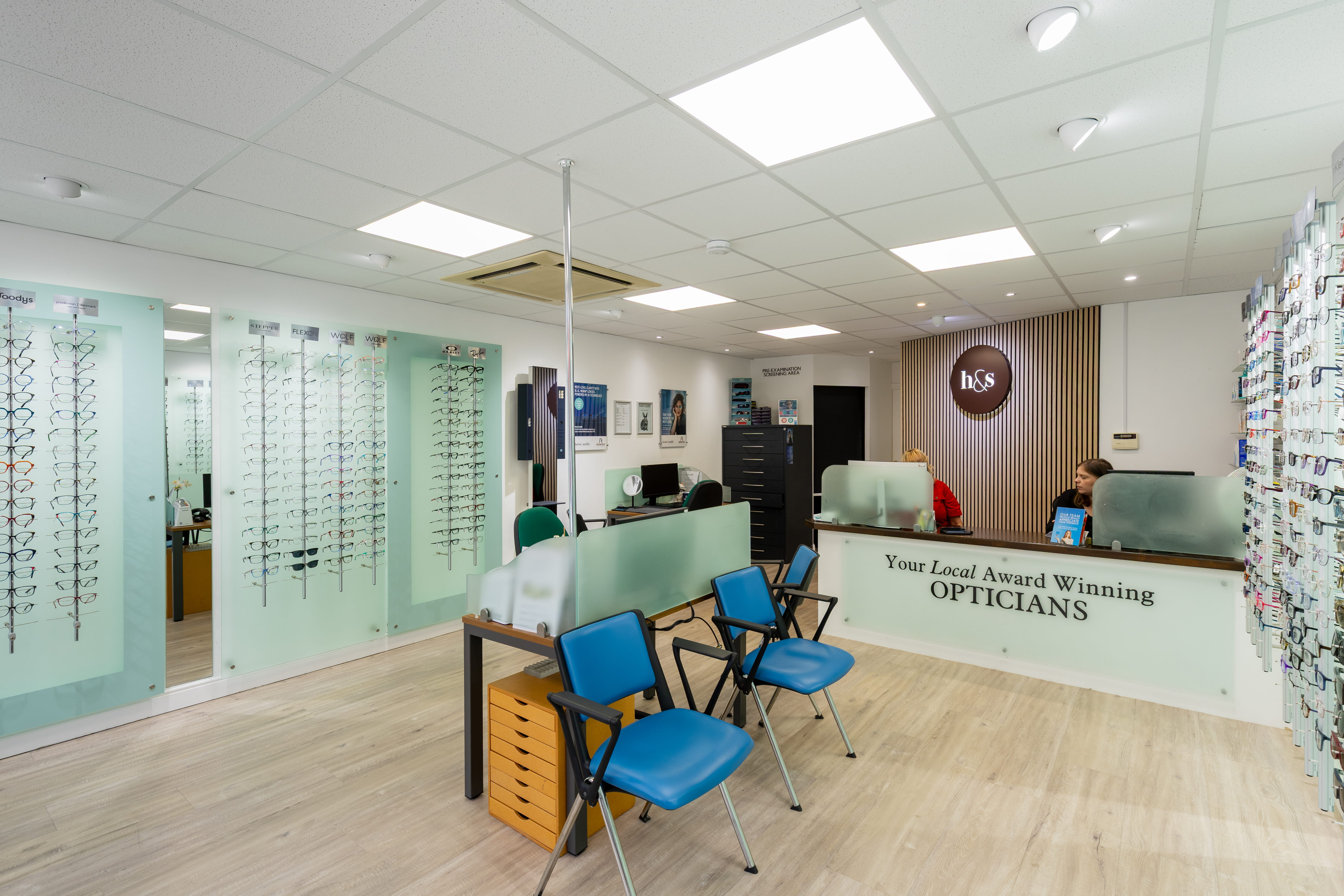 Bright and modern Haine & Smith Opticians practice interior featuring eyewear displays, consultation desks, blue customer seating, and a reception area with staff assistance