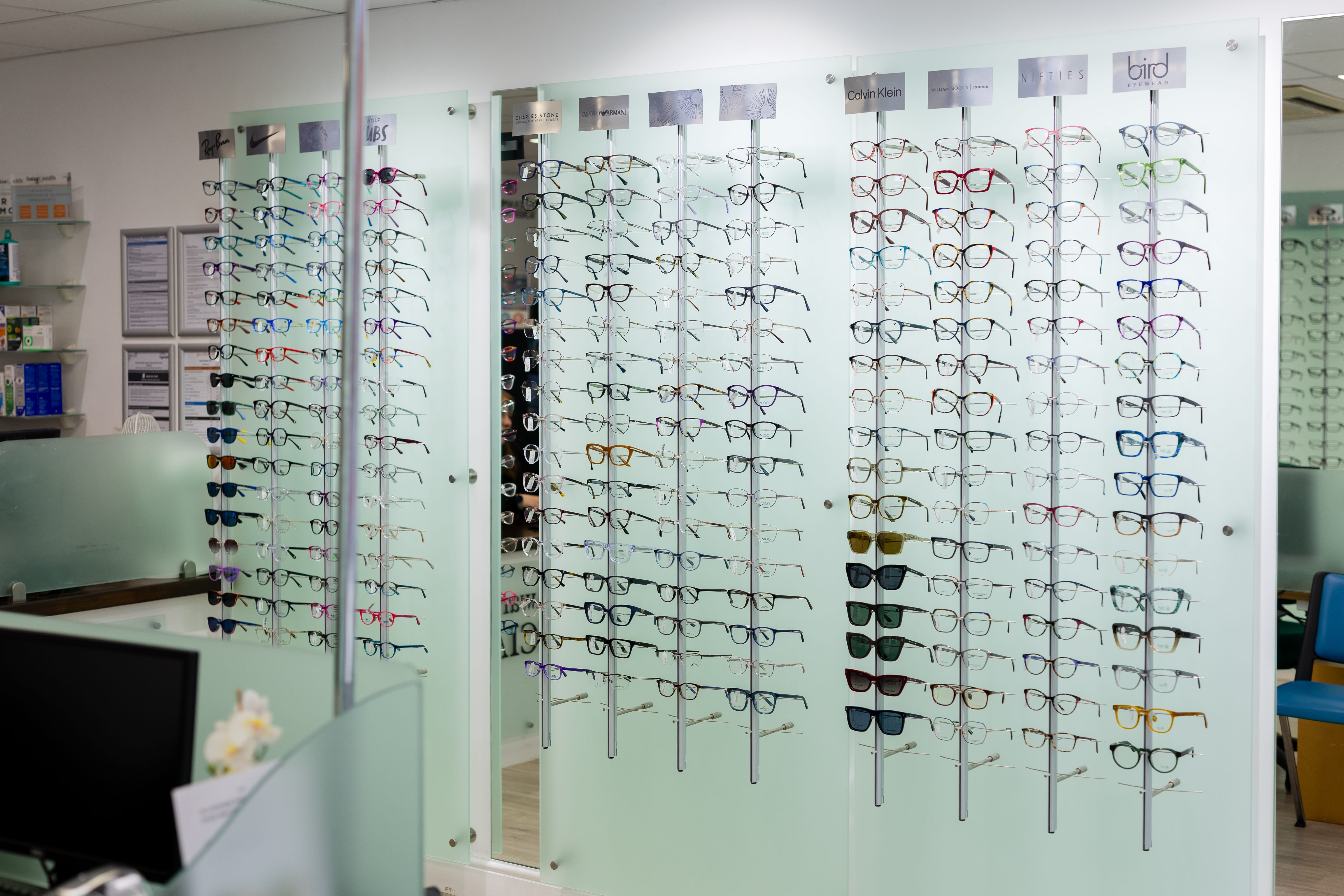 Wall-mounted eyewear display inside a Haine & Smith Opticians practice featuring a wide selection of prescription glasses and sunglasses from leading designer and independent eyewear brands