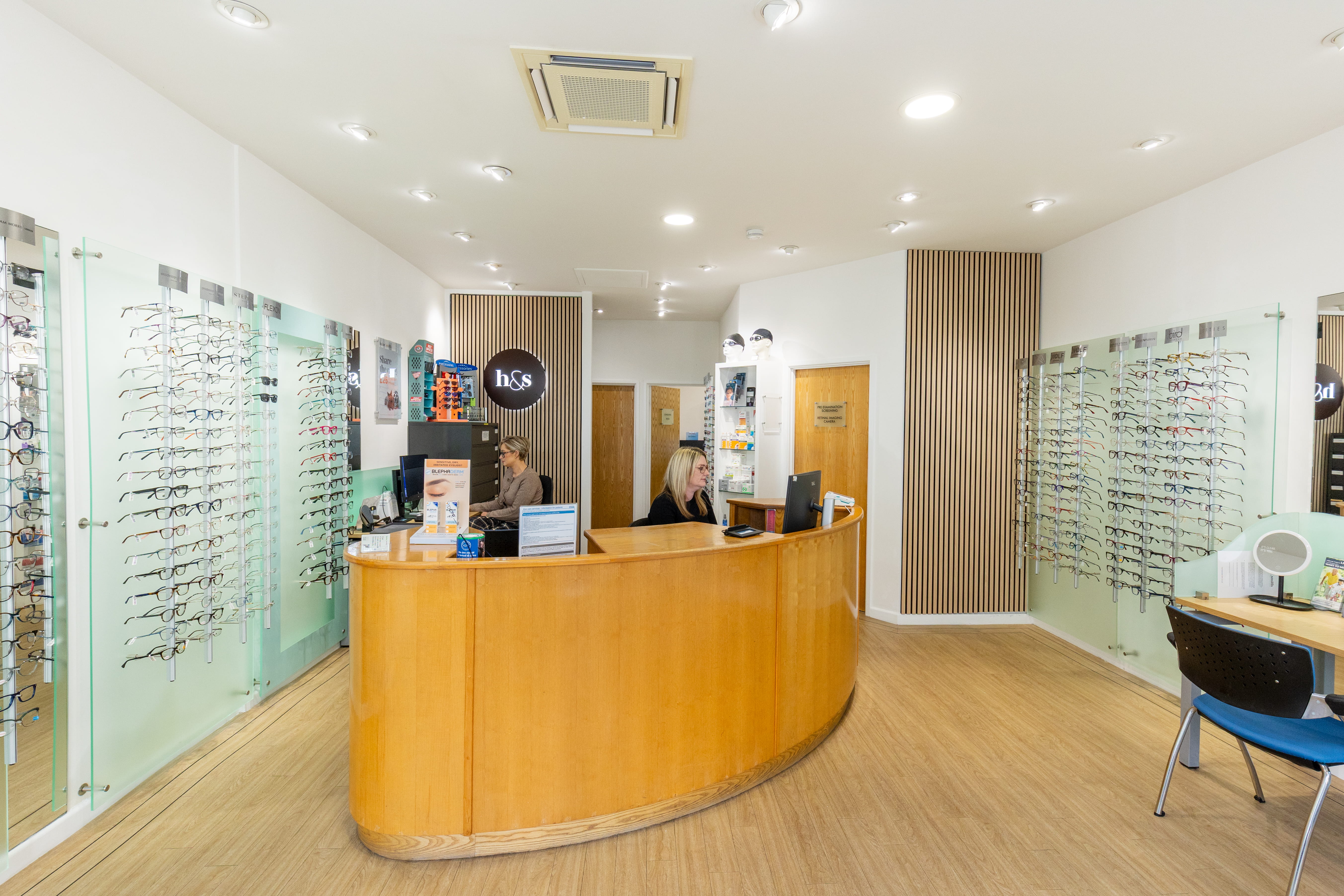 Bright and modern optician practice interior featuring a curved reception desk, eyewear displays, and staff assisting patients in a welcoming environment