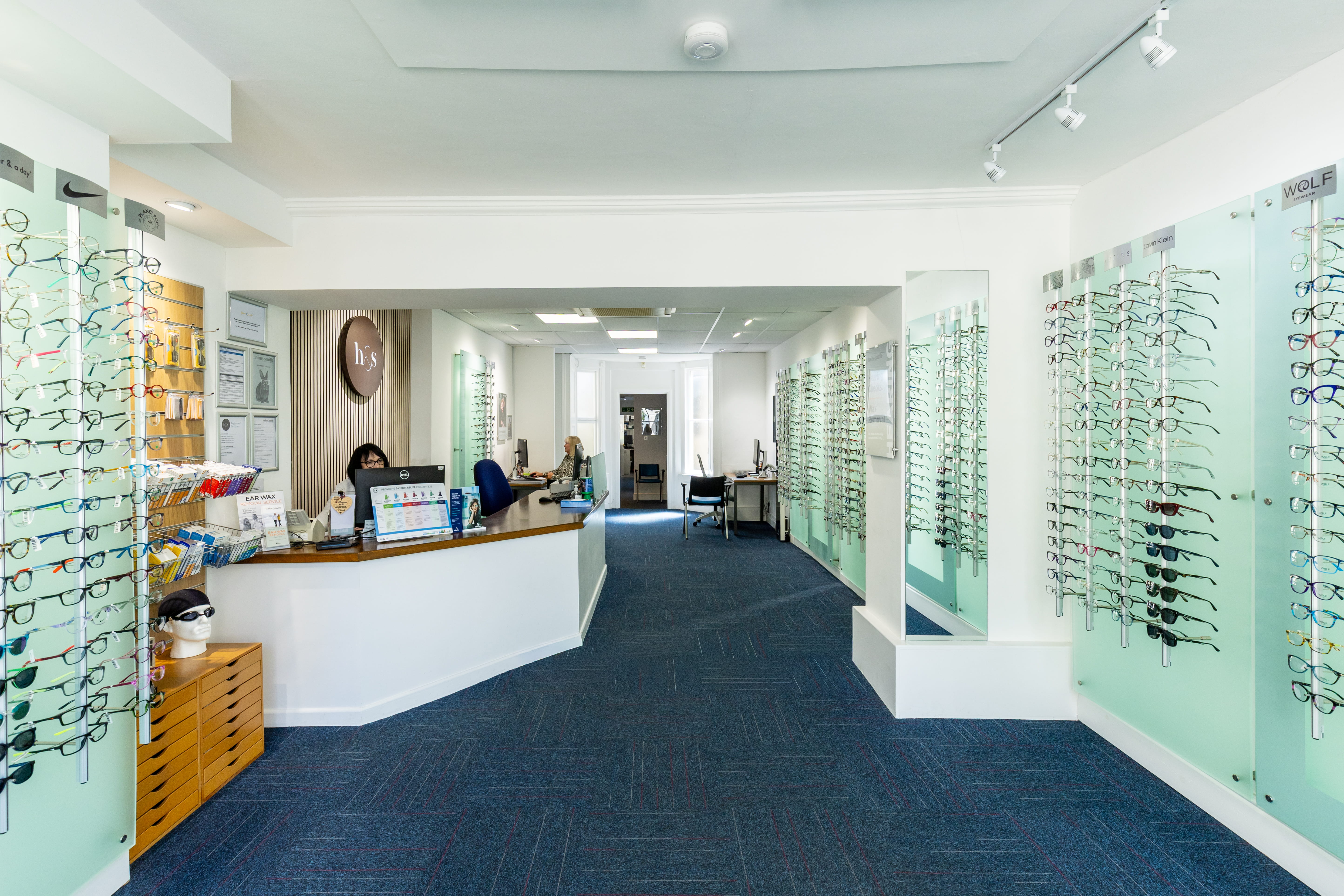 Spacious Haine & Smith Opticians practice interior featuring a reception desk, eyewear displays, consultation areas, and a wide selection of prescription glasses and sunglasses in a bright, modern setting