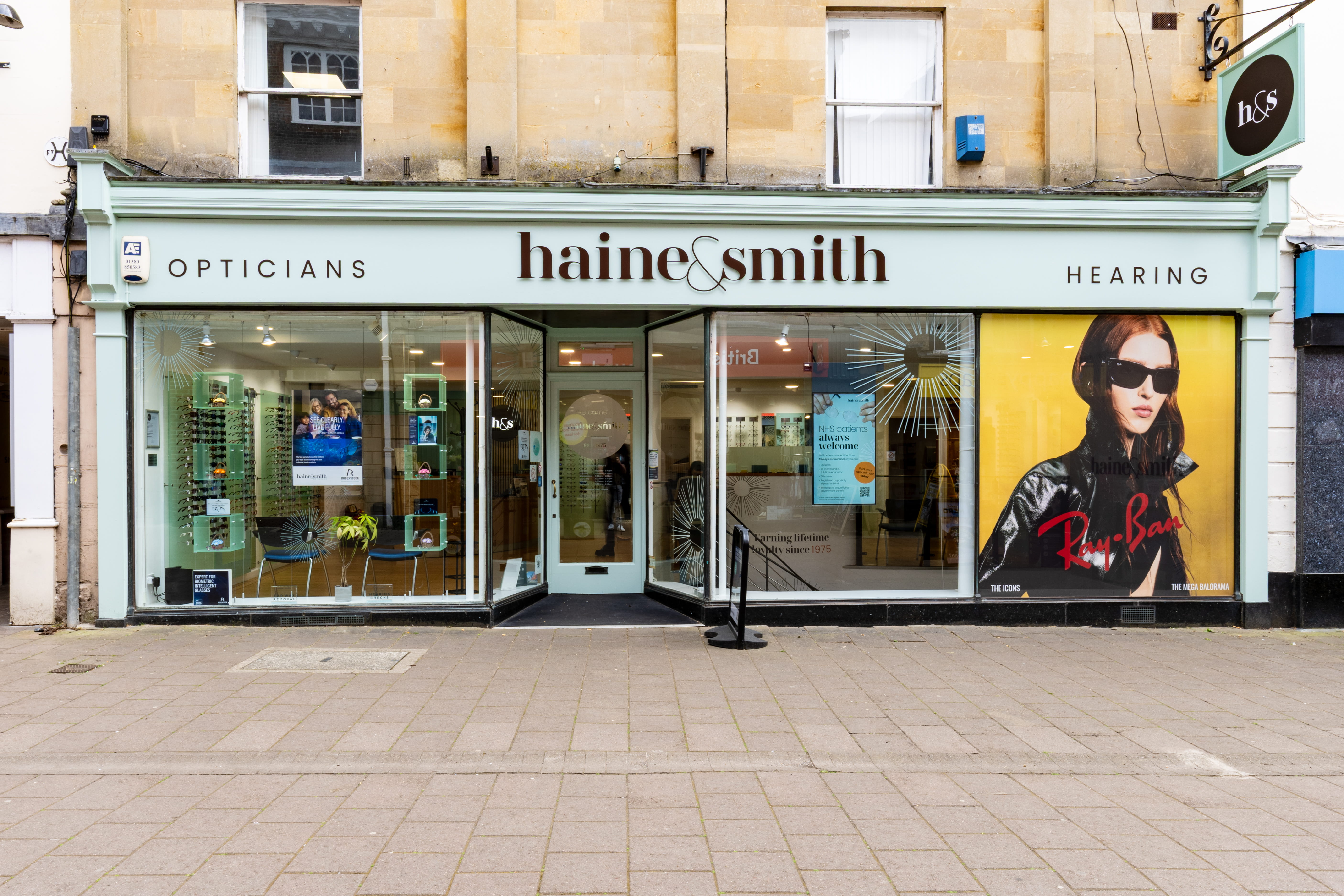 Exterior view of a Haine & Smith Opticians and Hearing Care practice, featuring large display windows, eyewear collections, and modern high street storefront branding