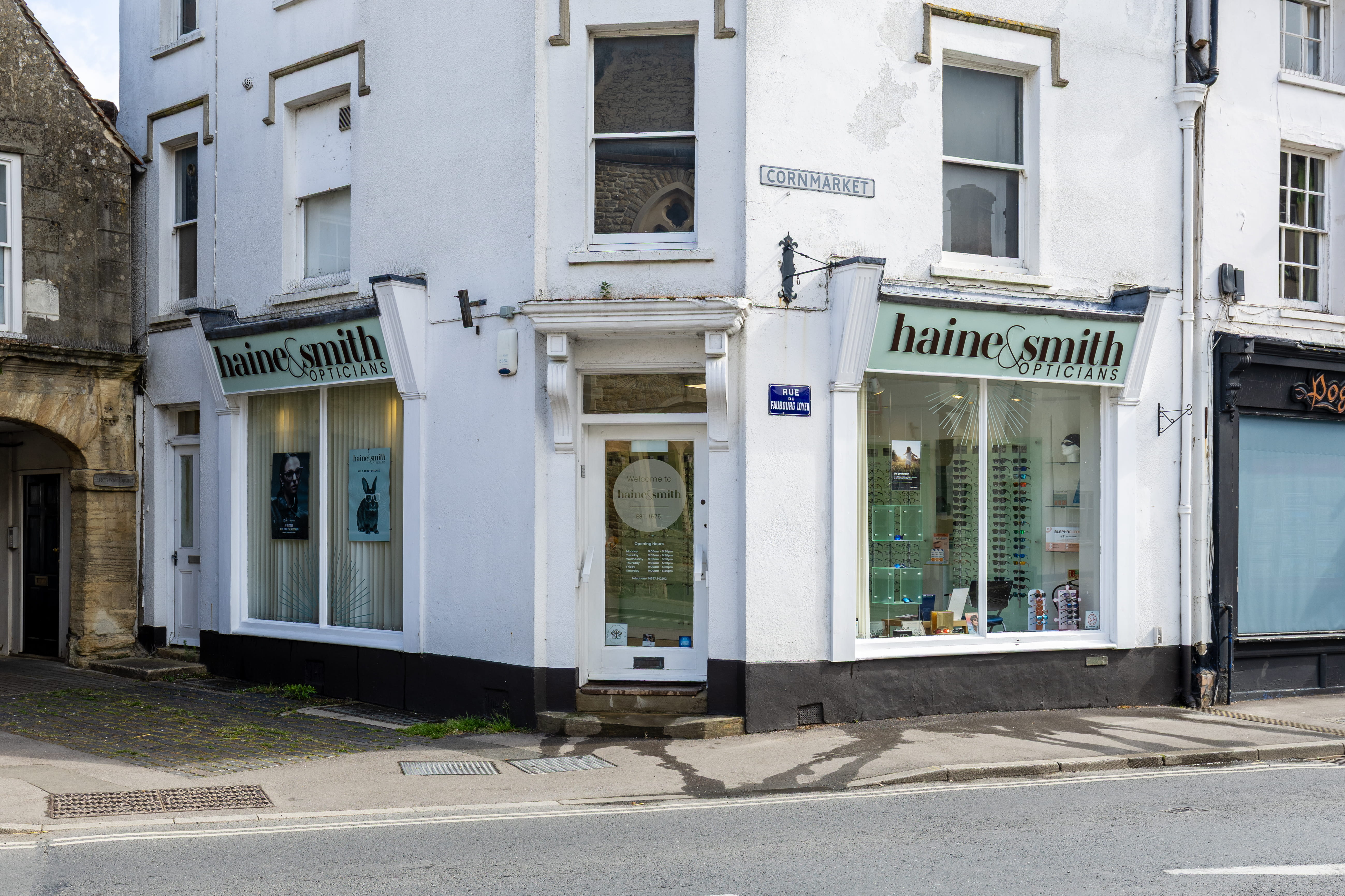 Exterior view of a Haine & Smith Opticians practice on a street corner, featuring large display windows, branded signage, and a welcoming entrance in a historic town centre setting