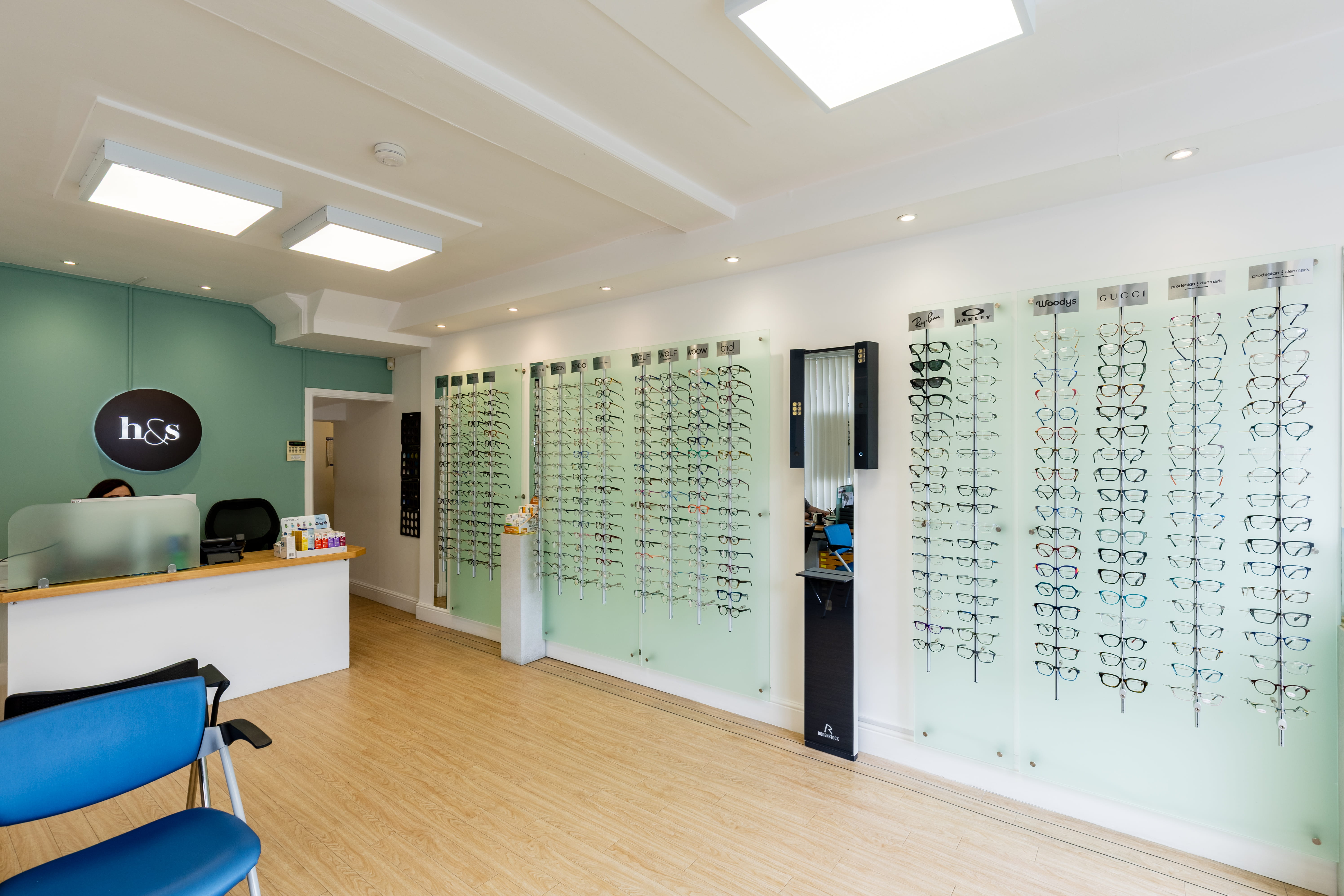 Bright and modern opticians practice interior featuring a reception desk, waiting area, and wall-mounted displays of designer eyeglass frames in a spacious showroom