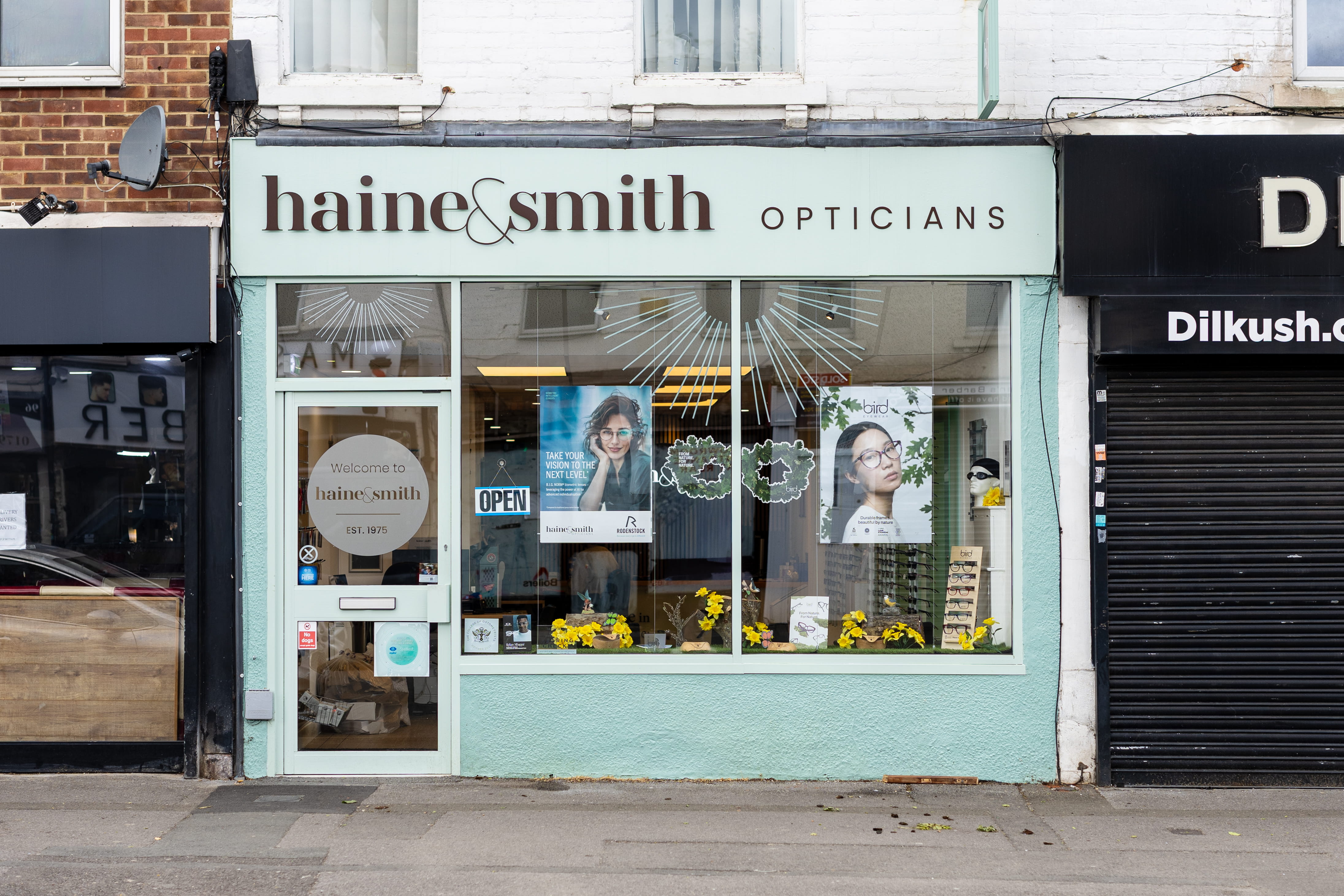 Front exterior of Haine & Smith Opticians featuring branded storefront signage, large display windows with eyewear promotions, and a welcoming high street practice entrance