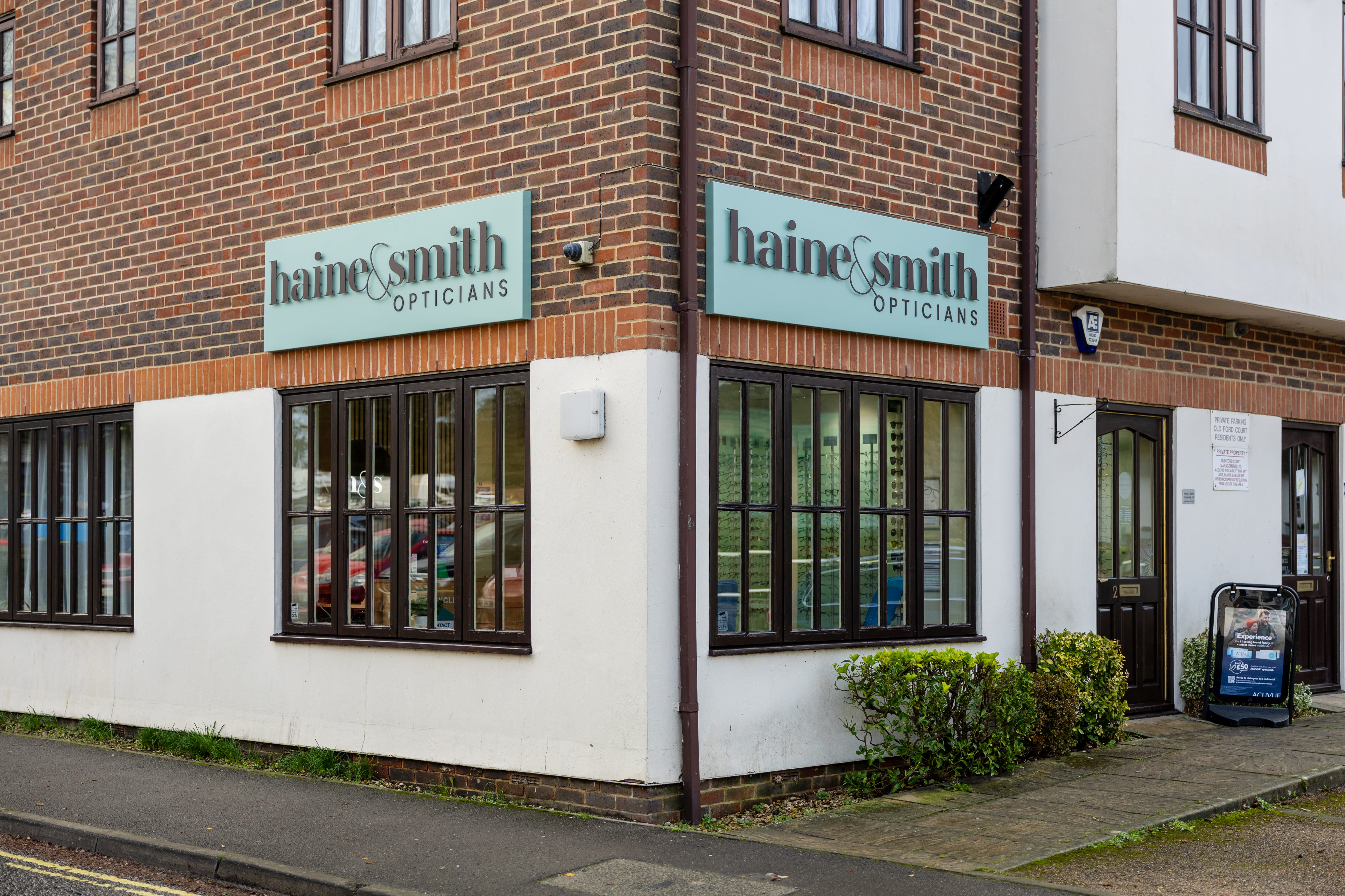 Exterior view of Haine & Smith Opticians on a corner brick building, featuring branded signage, large windows showcasing eyewear displays, and a welcoming entrance to the practice