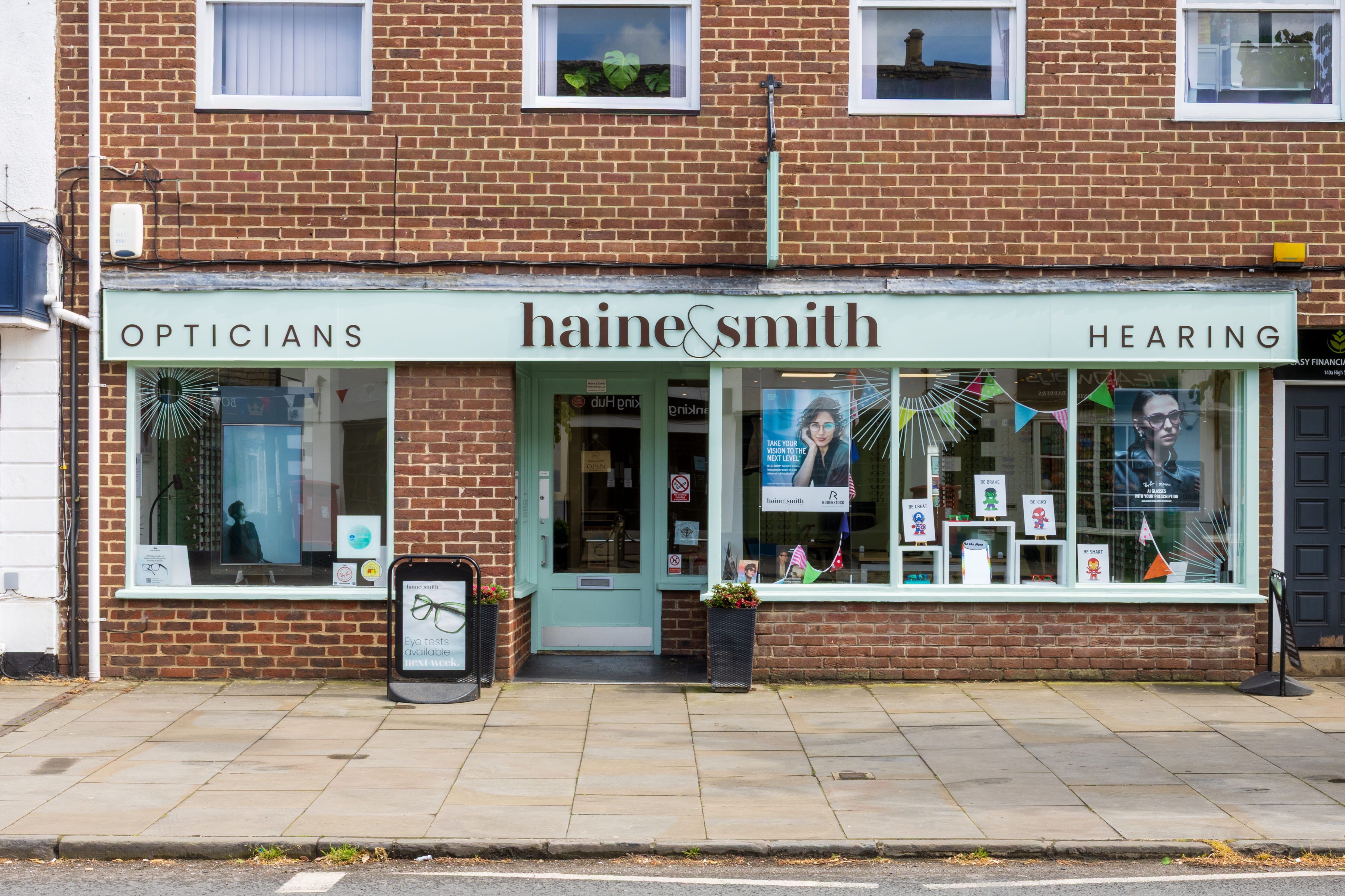 Front exterior of Haine & Smith Opticians and Hearing practice, featuring large display windows with eyewear promotions, branded signage, and a welcoming high street storefront