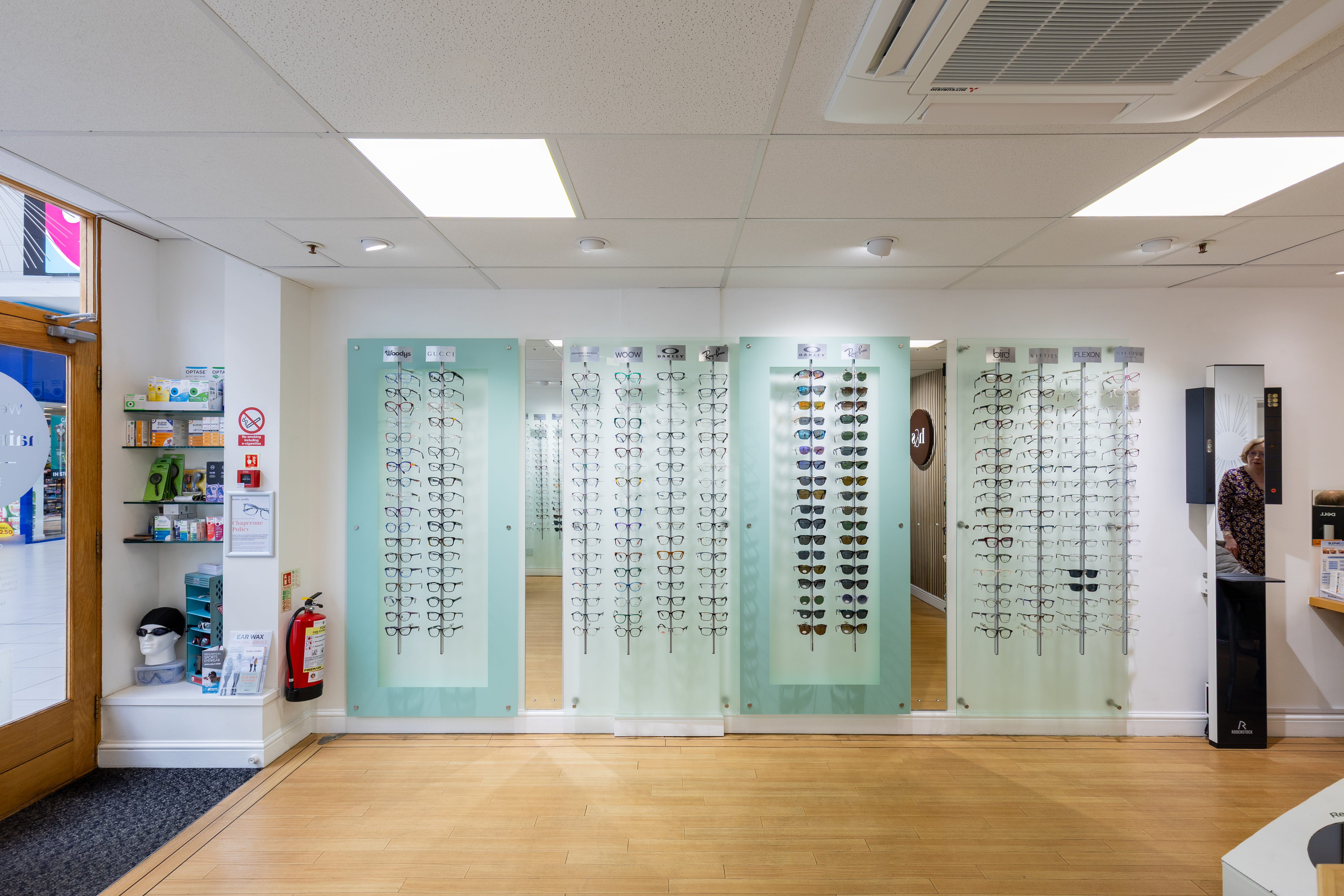 Interior of a Haine & Smith Opticians practice featuring wall-mounted displays of prescription glasses and sunglasses, wooden flooring, and a bright, modern showroom layout