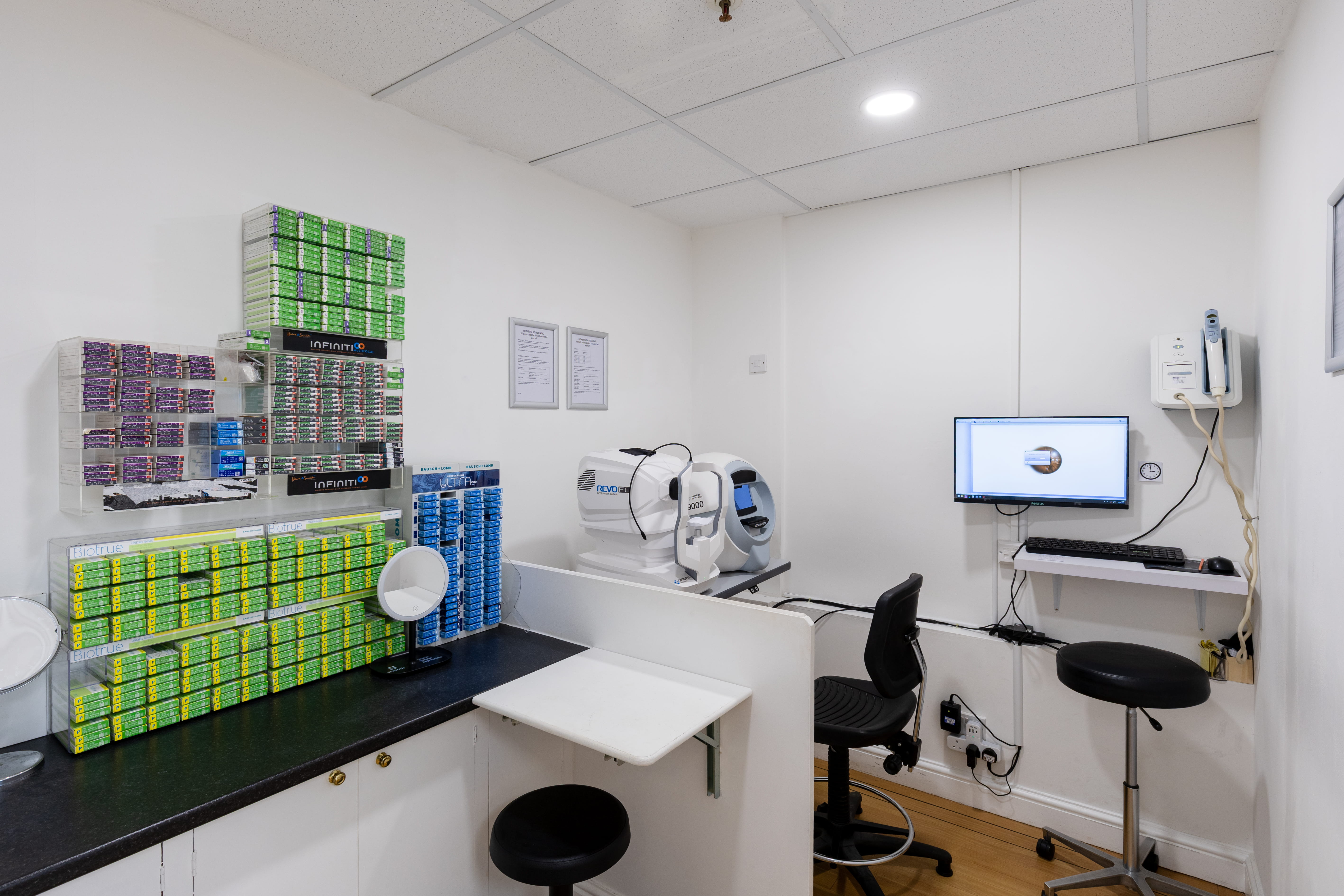 Modern opticians consultation room with contact lens supplies, diagnostic eye testing equipment, a computer workstation, and seating for patient eye care appointments