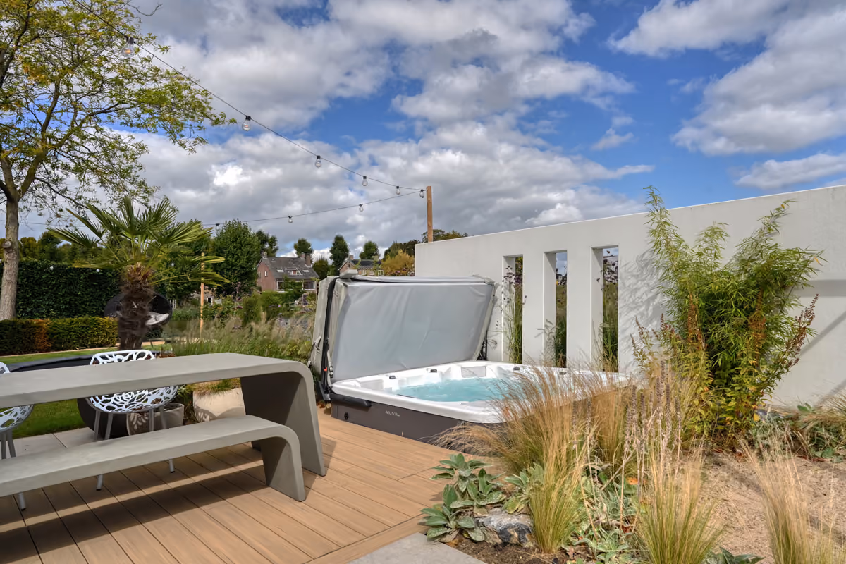 Tuin met moderne houten picknickbank, jacuzzi, planten en een partly bewolkte blauwe hemel.