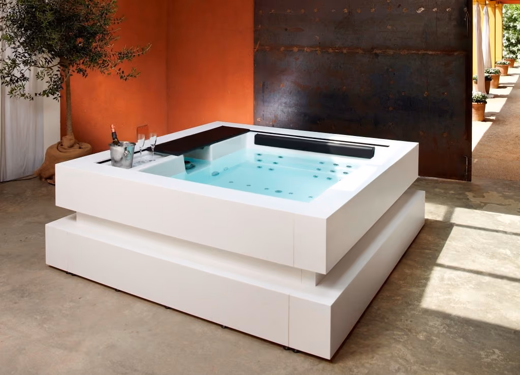 Moderne witte jacuzzi in binnenruimte met champagne, glazen en olijfboom naast oranje muur.