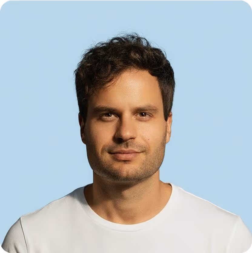A man with dark hair wearing a white t-shirt is looking directly at the camera.

