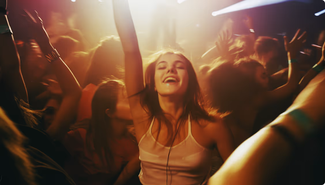 A woman joyfully dances at a party, raising her hands in celebration amidst a lively atmosphere.