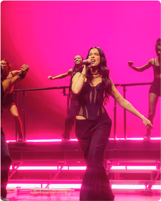 Dua Lipa performing with backup dancers in front of vibrant pink stage lighting