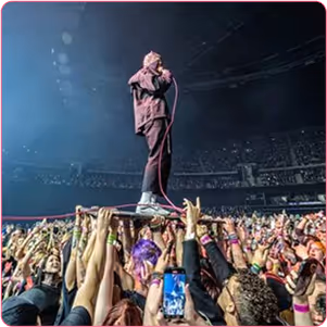 Masked performer standing on a crowd with microphone in hand and singing
