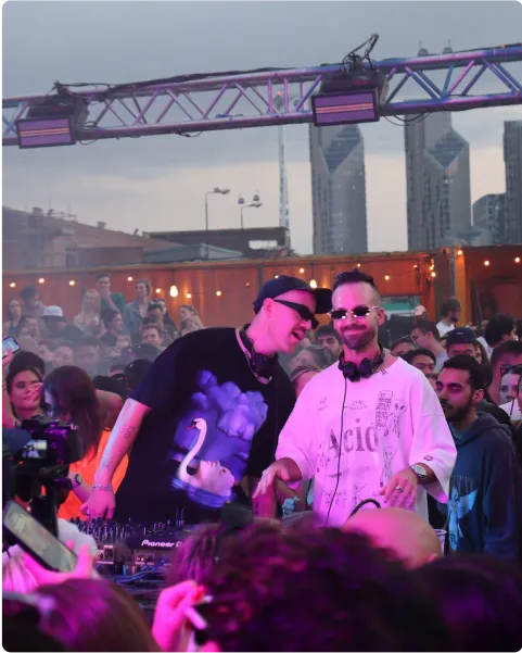 Two DJs performing for a crowd at an outdoor music event.