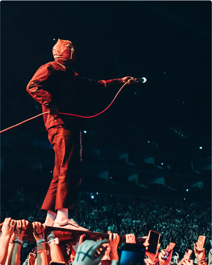 Masked performer standing on a crowd with microphone in hand
