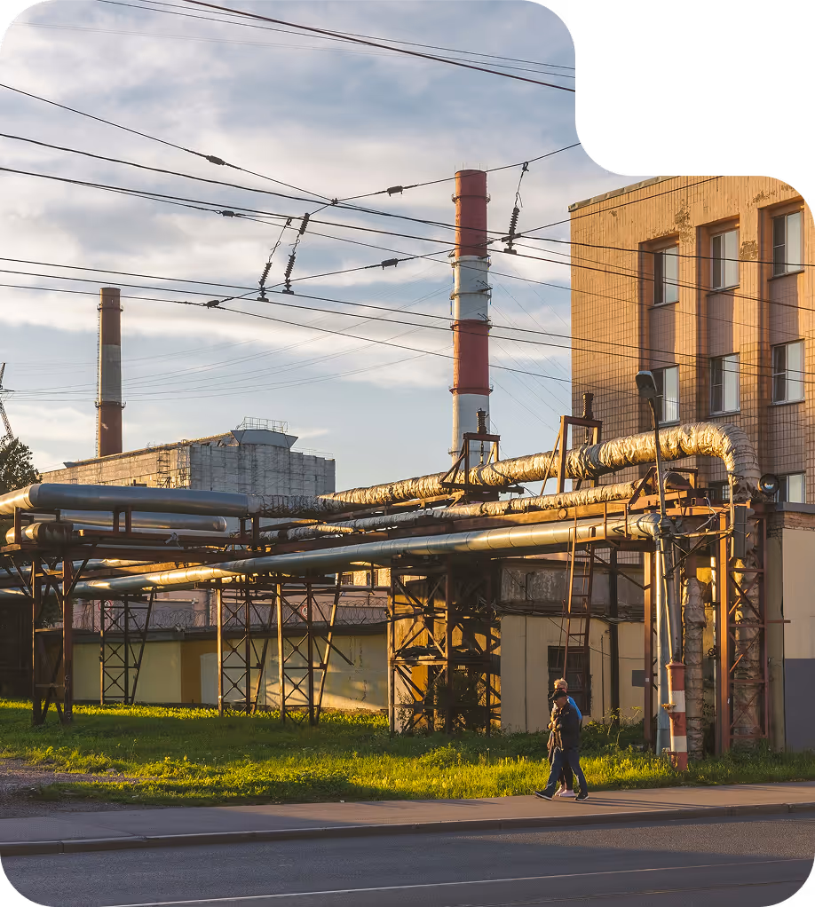 Industrial facility with exposed pipelines, buildings, and smokestacks, with a person walking in the foreground