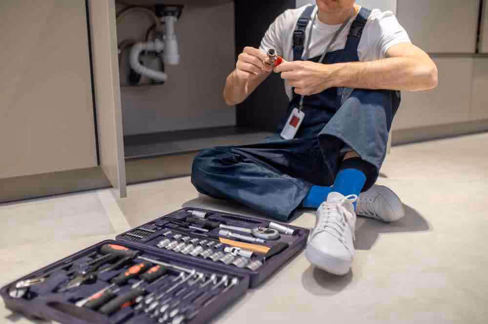 A plumber with his plumbing tools in a residential kitchen plumbing job.