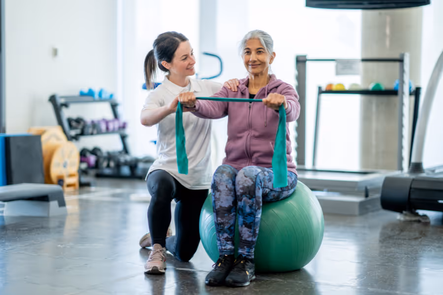 A phsyiotherapist helping an older patient through hip pain on a bosu ball and stretchy band exercise