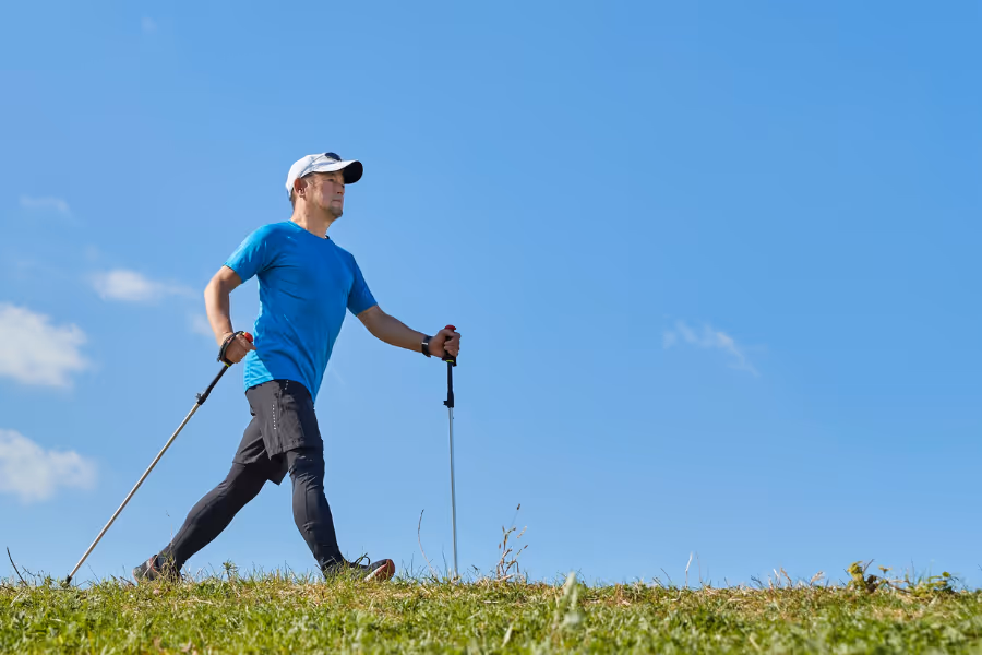 Man walking vigorously post hip replacement surgery with walking poles on a blue sky day. 