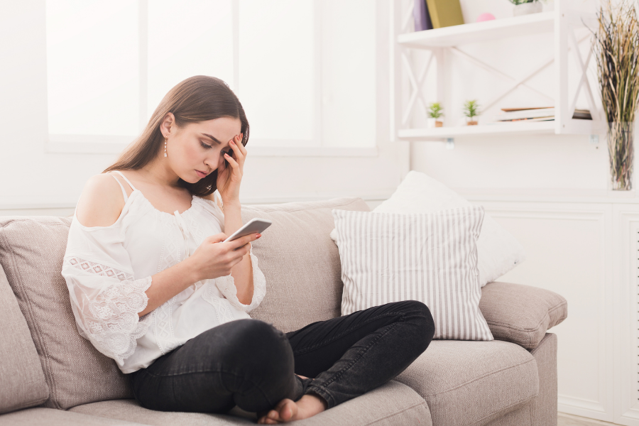 Woman sitting on couch cross legged, looking anxious as she reads about urinary incontinence
