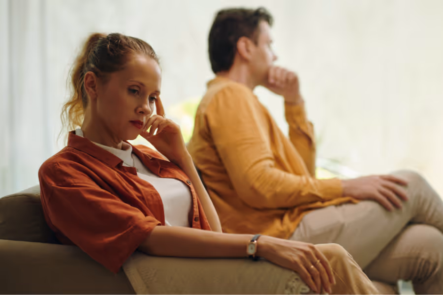 Man and woman looking stressed sitting next to each other on neutral tone couch