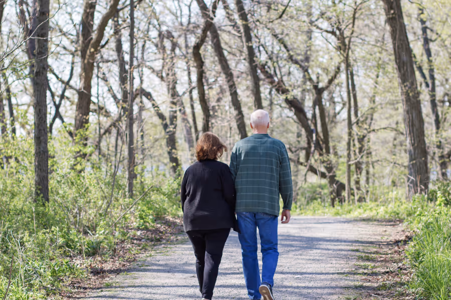 Older couple walking hand in hand down a forest path months after a hip replacement surgery