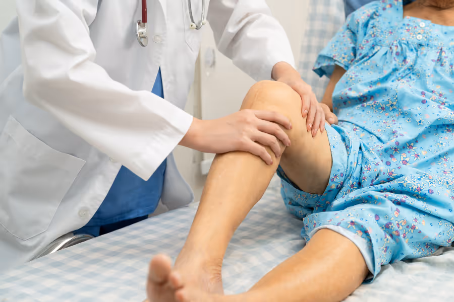 Patient with a knee replacement scar, a year later, on a medical bed, being inspected by a surgeon