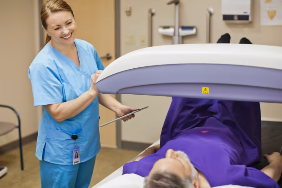 Private clinician smiling, helping patient into DEXA scan position
