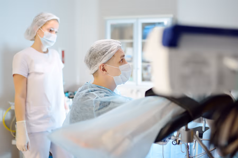 General surgeon removing a cyst in an operating room while clinician watches on